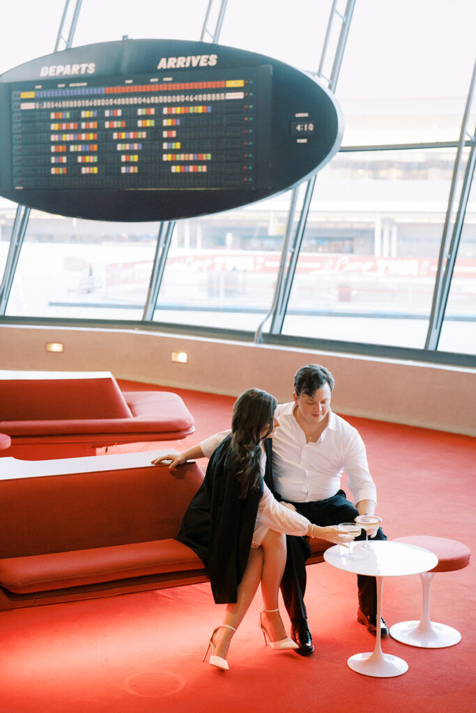 NYC Engagement Photos at TWA Hotel with couple holding champagne