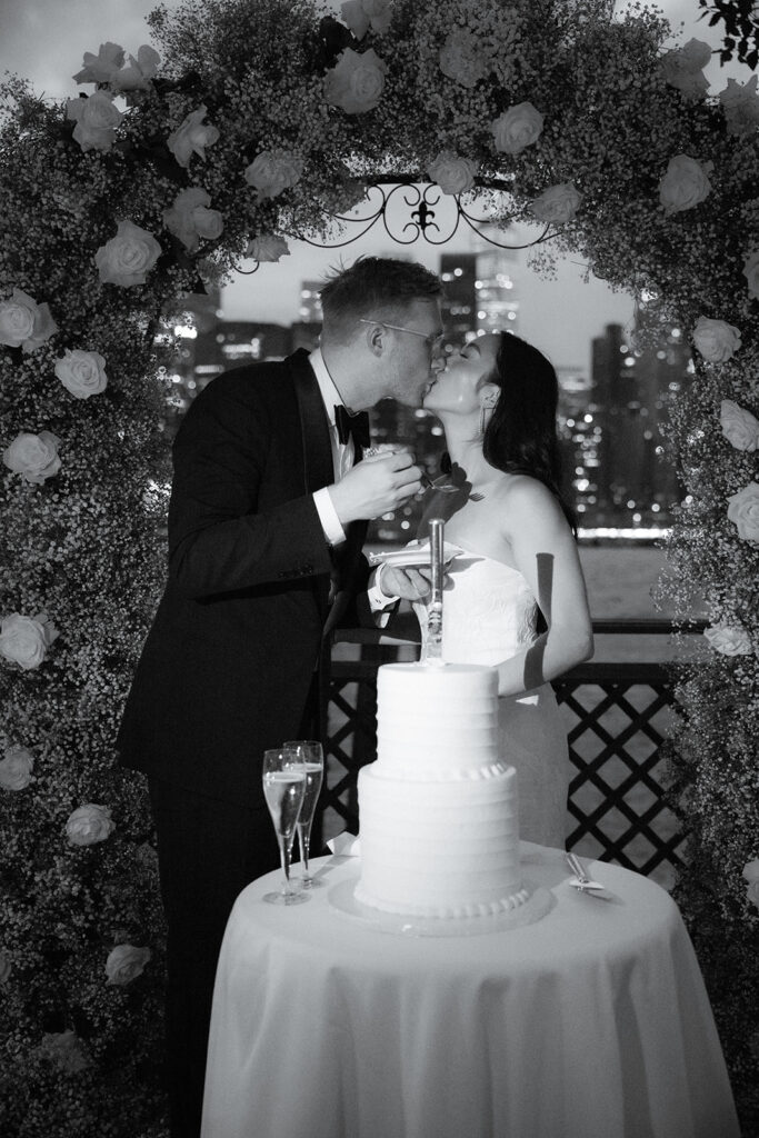 Couple kissing and cutting cake at their reception at the River Cafe in Brooklyn